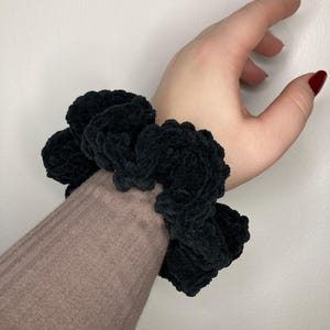 Può includere: Un elastico per capelli nero e soffice con un grande design soffice e testurizzato.