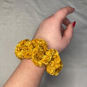 Può includere: Un elastico per capelli in velluto giallo fatto di tessuto all'uncinetto. L'elastico è indossato al polso di una persona.