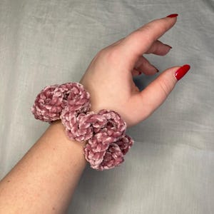 Può includere: Un elastico per capelli in velluto rosa con un doppio nodo.