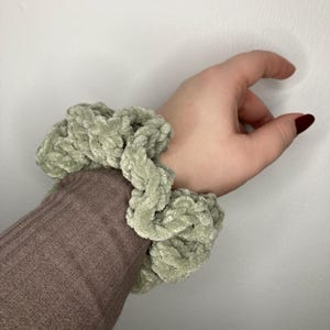 Può includere: Un elastico per capelli verde salvia fatto di filato morbido e peloso. Lo scrunchie è annodato ed è pronto per essere indossato.