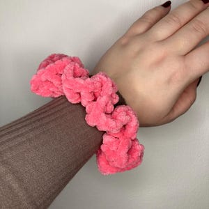 Può includere: Un elastico per capelli rosa e peloso fatto di filato.