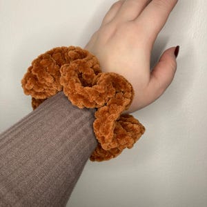 Può includere: Un elastico per capelli marrone e peloso. L'elastico è fatto di un materiale morbido e soffice ed è annodato.
