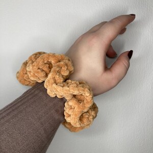 Può includere: Un elastico per capelli color marrone lavorato a uncinetto con una texture soffice.