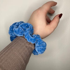 Può includere: Un elastico per capelli blu e peloso fatto di filato.