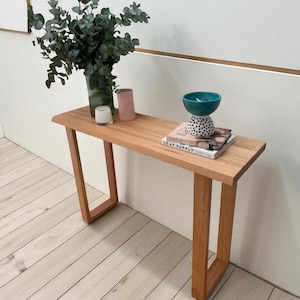 Op de afbeelding: Een lichtbruine houten consoletafel met een rechthoekig blad en schuine poten. De tafel is versierd met een vaas met groen, kaarsen, boeken en een turquoise kom. De tafel is 122 cm lang.