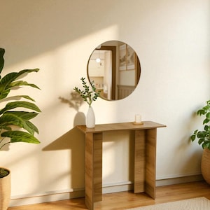May include: A wooden console table with a circular mirror above. A white vase with greenery and a small candle are on the table. Potted plants are in the foreground and background, creating a warm, inviting space.