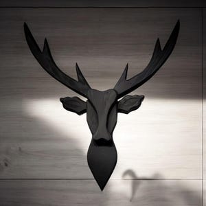 Puede incluir: Una cabeza de ciervo de madera negra montada en una pared. La cabeza de ciervo es una pieza decorativa con un diseño simple.