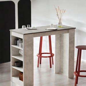 May include: A modern kitchen island with a gray countertop and built-in shelving. Two red bar stools are positioned near the island. The island has a built-in shelf with dishes and glassware. A vase with dried plants sits on the countertop.