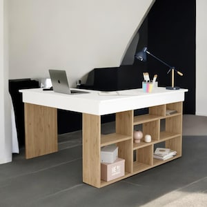 Puede incluir: Un escritorio moderno blanco y madera con estanterías integradas. El escritorio tiene una parte superior blanca y patas y estanterías de madera clara. Una computadora portátil, una lámpara y útiles de oficina están sobre el escritorio.