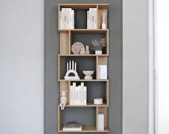 Puede incluir: Estantería asimétrica de madera clara montada en una pared gris, llena de objetos decorativos. Los estantes exhiben libros, velas, jarrones y pequeñas esculturas. La estética general es minimalista y moderna.
