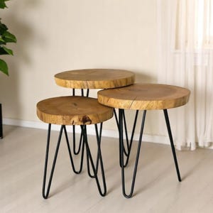 May include: Three round wooden coffee tables with black metal hairpin legs. The tables are nested together, with the largest table on the bottom and the smallest table on top.
