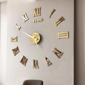 May include: A gold-toned, 3D, Roman numeral clock with a white clock hand and a gold-toned center. The clock is mounted on a white wall.