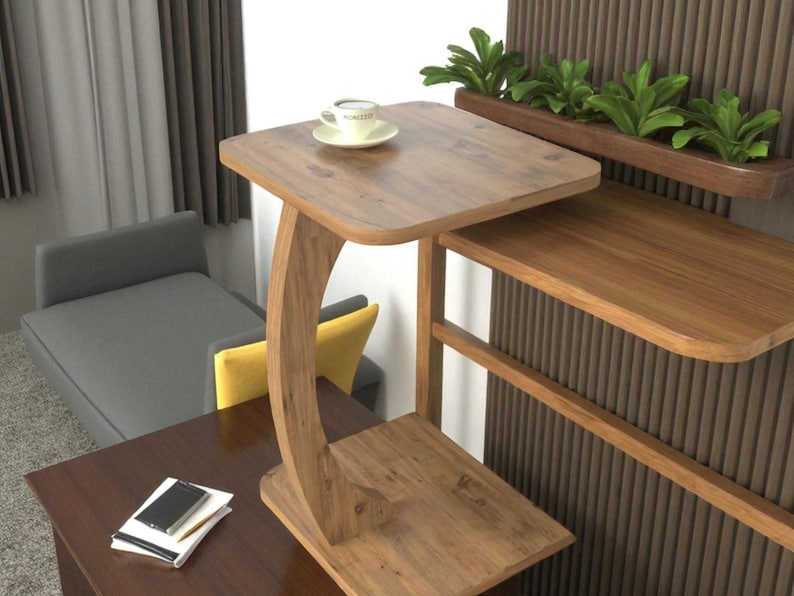 Pu&ograve; includere: Un tavolino in legno con una gamba curva e due livelli. Una tazza di caff&egrave; &egrave; appoggiata sul livello superiore. Il tavolo &egrave; in legno marrone chiaro e ha un design moderno. Il tavolo &egrave; alto circa 61 cm.