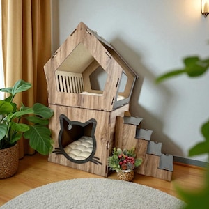 May include: A two-storey wooden cat house in a house shape. It features a cat-face entrance, a small staircase, and a window. The interior has a bed. The cat house is made of light brown wood. The measurements are in centimeters.