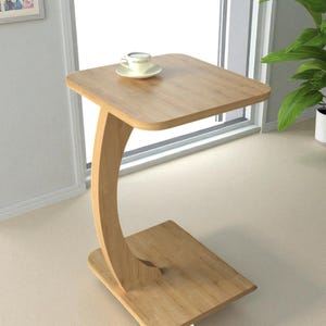 Pu&ograve; includere: Un tavolino in legno chiaro con piano quadrato e gamba curva. Una tazzina da t&egrave; e un piattino sono appoggiati sul tavolo. Il tavolo &egrave; alto circa 61 cm.