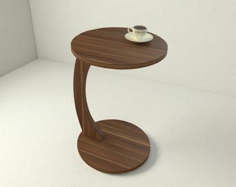 May include: A dark brown, C-shaped side table with a round top and base. A small white teacup and saucer sit on the table's surface. The table is made of wood and has a modern design.