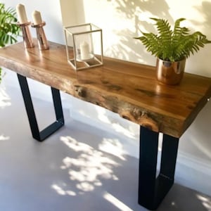 May include: A rustic wooden console table with a live edge top and black metal hairpin legs. The table is decorated with candles and a potted plant.