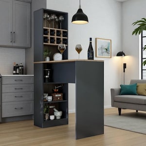 Op de afbeelding: Een donkergrijs keukeneiland met een wijnrek, planken en een houten aanrecht. Wijnglazen, een fles wijn en een klok staan op het aanrecht. Het eiland staat in een moderne keuken met een grijze bank en een groot raam.