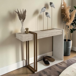 May include: A contemporary console table with a white, textured top and gold-coloured metal legs. Decorative bird sculptures on thin metal rods are displayed on the table. A vase with dried plants and a potted plant are also visible.