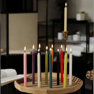 May include: A wooden tray with a variety of colored candles, including pink, purple, cream, green, teal, black, red, yellow, and white. The candles are lit and are arranged in a circle on the tray.