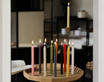 May include: A wooden tray with a variety of coloured candles, including pink, purple, cream, green, teal, black, red, yellow, and white. The candles are lit and are arranged in a circle on the tray.