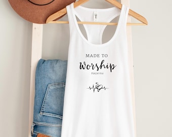 May include: White tank top with the text "MADE TO Worship" and Psalm 95:6 printed in black. A musical note and heartbeat graphic is below the text. A brown hat and blue jeans are in the background.