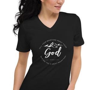 May include: Black V-neck t-shirt with a white graphic. The graphic features a mountain range and the word "God" in a stylized font, surrounded by text. The shirt is made of a soft material.