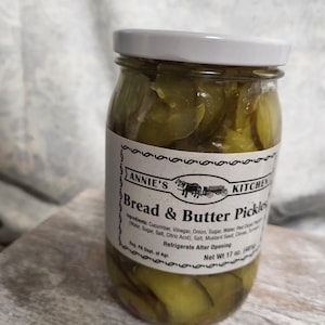 May include: A jar of Annie's Kitchen Bread & Butter Pickles. The jar has a white lid and a label with the product name and ingredients. The jar contains sliced green pickles. Net weight is 17 oz.