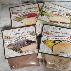 Könnte beinhalten: Vier Käsekuchen-Mix-Packungen von Halladay's Harvest Barn. Geschmacksrichtungen sind Lemon Raspberry, Key Lime, Mocha Latte und Pumpkin. Jede Packung zeigt ein Bild des fertigen Desserts und die Worte "No Bake!" und "Recipes Inside!"