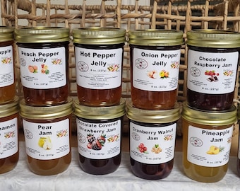 May include: A selection of glass jars filled with different jellies, such as apricot pineapple, peach pepper, and chocolate raspberry. Each jar has a gold lid and a label with the flavour name and a graphic. Each jar contains 227g of jelly.