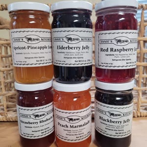 May include: Six glass jars of homemade jam and jelly, labeled with the name "Annie's Kitchen". The flavors are Apricot-Pineapple Jam, Elderberry Jelly, Red Raspberry Jam, Strawberry Rhubarb, Peach Marmalade, and Blackberry Jelly.