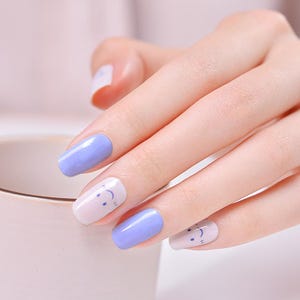 Könnte beinhalten: Nahaufnahme einer Hand mit hellblauem und weißem Nagellack. Die weißen Nägel haben ein kleines blaues Smiley-Gesicht-Design.