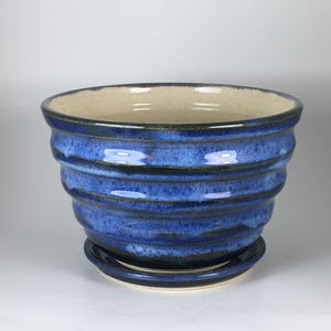 May include: A round ceramic planter with a vibrant blue glaze and horizontal ribbed texture. The pot features a wide opening, a light-colored interior, and comes with a matching circular saucer base, creating a cohesive look for indoor plant display.