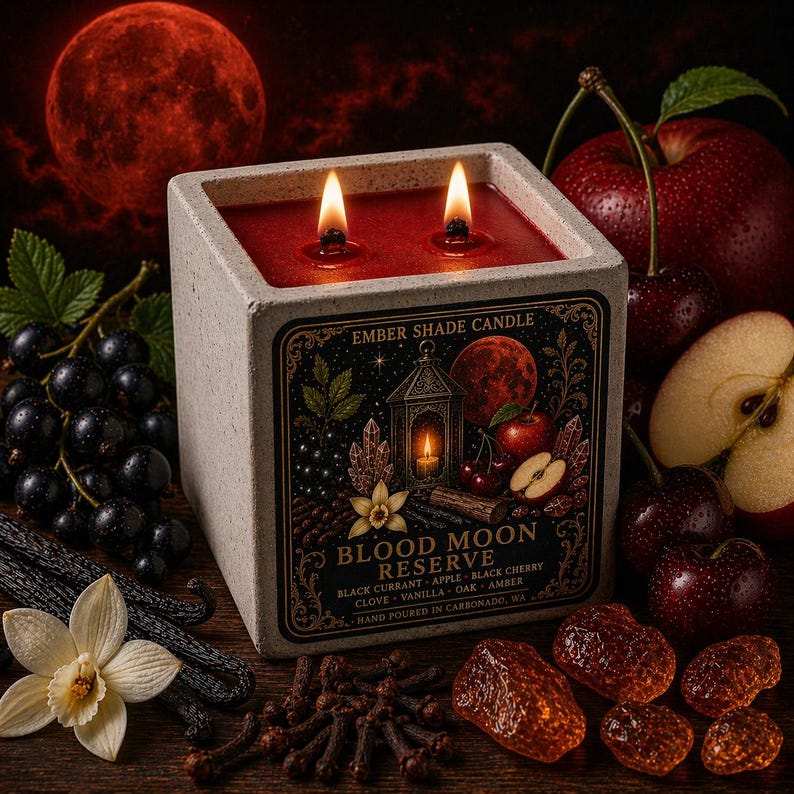 May include: A square, lit candle with the text "Blood Moon Reserve" on the label. The candle is surrounded by cherries, apples, cloves, vanilla, and other ingredients. A large red moon is in the background.