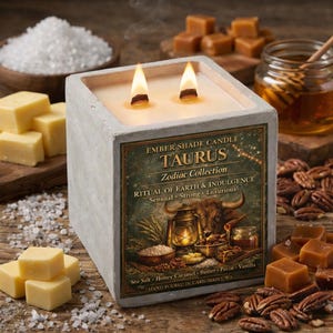 May include: A square concrete candle with two lit wicks. The label reads "TAURUS Zodiac Collection" with the words "Sensual, Strong, Luxurious". Surrounding the candle are caramel squares, pecans, salt, and honey.