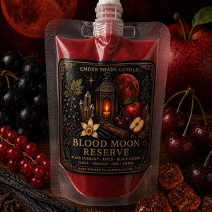 May include: A pouch of red liquid with a label reading "Blood Moon Reserve" by Ember Shade Candle. The label features illustrations of a lantern, crystals, and fruit. Ingredients listed include black currant, apple, and black cherry. The background includes fruit and a red moon.