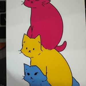 May include: A vertical illustration featuring three stacked cats. The top cat is bright pink with closed eyes, the middle cat is yellow with wide eyes, and the bottom cat is light blue with narrow eyes. All cats have black outlines.