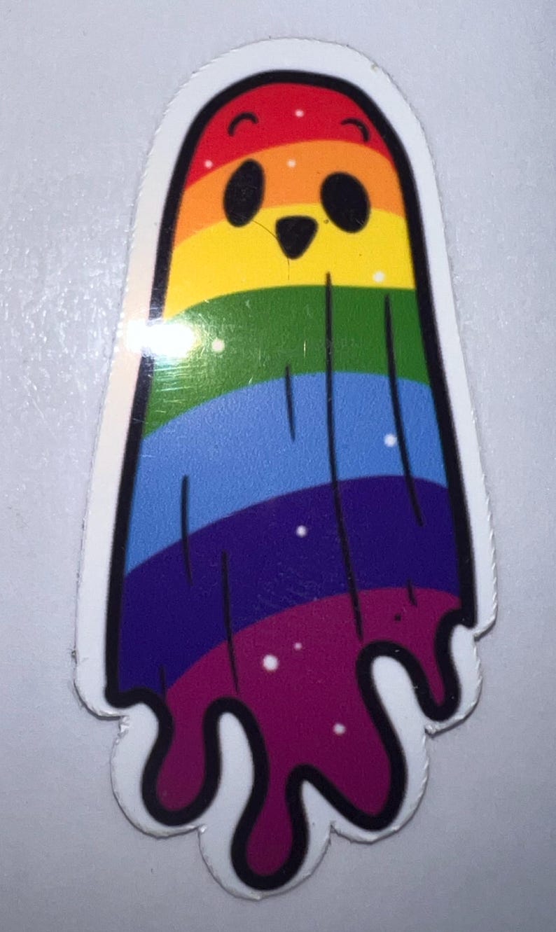 K&ouml;nnte beinhalten: Ein farbenfroher Aufkleber mit einem Cartoon-Geist in Regenbogenfarben. Der Geist hat ein schwarzes Gesicht mit zwei Augen und einem kleinen Mund. Die Regenbogenfarben umfassen Rot, Orange, Gelb, Gr&uuml;n, Blau, Lila und Rosa. Der Geist hat einen wei&szlig;en Rand.