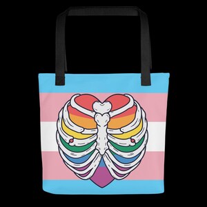 May include: Tote bag with a heart-shaped, rainbow-coloured rib cage design on a transgender pride flag background. The bag has black handles and is suitable for carrying items.