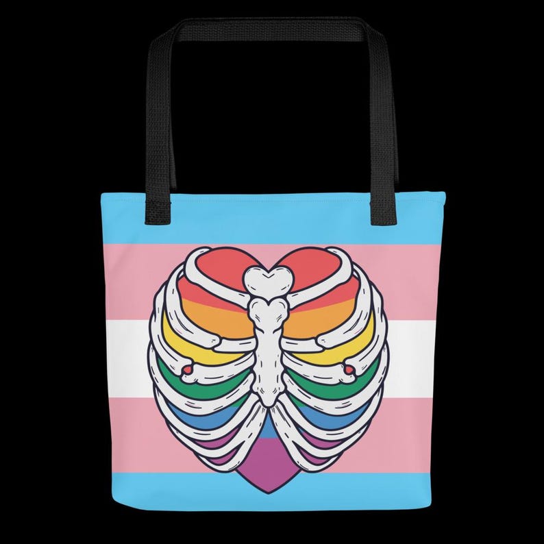 May include: Tote bag with a heart-shaped, rainbow-coloured rib cage design on a transgender pride flag background. The bag has black handles and is suitable for carrying items.