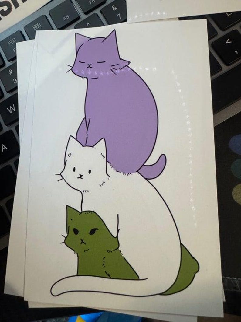 May include: A rectangular sticker featuring a vertical stack of three illustrated cats. The top cat is light purple with closed eyes, the middle cat is white with black eyes, and the bottom cat is olive green with a focused expression and black outlines.