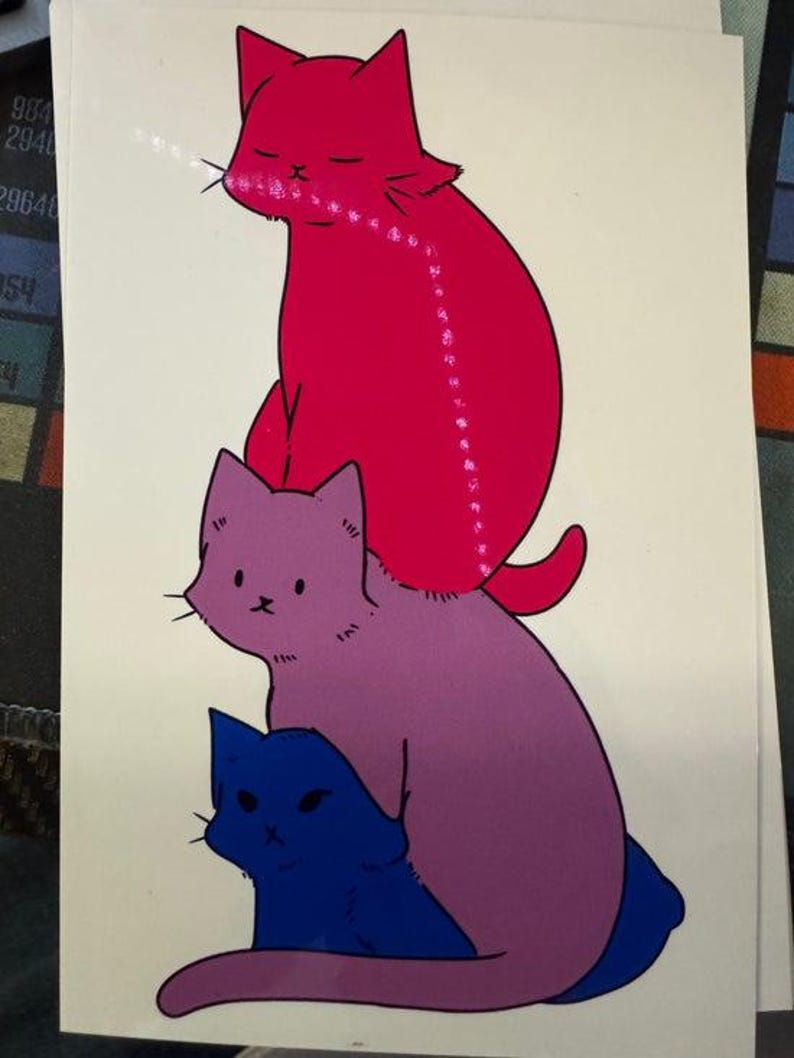 May include: A vertical illustration on a white background featuring three stacked cats. The top cat is bright pink, the middle cat is purple, and the bottom cat is dark blue. Each cat has simple facial features and a solid colour fill.