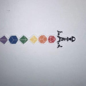Op de afbeelding: Een sticker met een zwaardontwerp waarbij het lemmet bestaat uit zes veelkleurige veelvlakdobbelstenen op een rij, waaronder paars, blauw, groen, geel, oranje en rood, bevestigd aan een zwart, sierlijk en gestileerd zwaardheft.