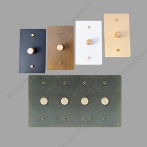 May include: A selection of rectangular and square light switch plates in colours such as black, brass, white, and gold. Each plate has a brass knob and screws. A larger plate with four brass knobs is also included.