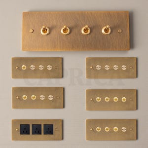 May include: A selection of brass electrical switch plates and sockets. The plates are rectangular with a brushed finish. The switches are toggle style with gold-coloured levers. The sockets are black. The arrangement includes plates with 2, 3, 4, 5, and 6 switches.
