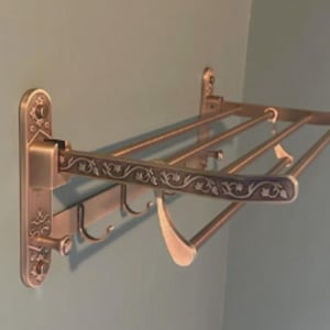 May include: A wall-mounted, antique-gold finished towel rack with three bars and decorative floral accents. The rack has four hooks on the bottom.