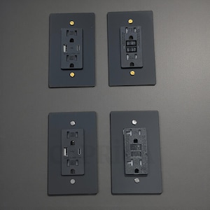 May include: Four black electrical outlet covers with various configurations. Two have standard outlets and USB ports, while the other two feature different outlet designs. Each cover is rectangular with rounded corners and secured with screws.