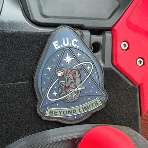 Pode incluir: Um patch com um design azul, preto e branco com o texto "E.U.C." e "BEYOND LIMITS". O patch retrata um ve&iacute;culo futurista com uma roda, contra um fundo de c&eacute;u estrelado.