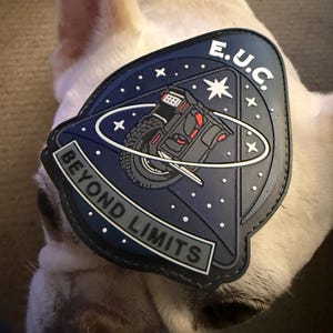 Pode incluir: Um patch azul marinho com o texto "BEYOND LIMITS" e "E.U.C." apresenta um gr&aacute;fico de um ve&iacute;culo. O patch est&aacute; definido contra o fundo de um c&atilde;o de cor clara.