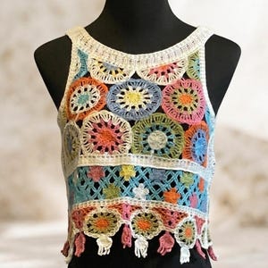 May include: A sleeveless crochet crop top featuring a colorful pattern of circular motifs in shades of pink, blue, yellow, orange, and green. The garment includes a white crocheted border at the neckline and hem, with small dangling fringe accents.
